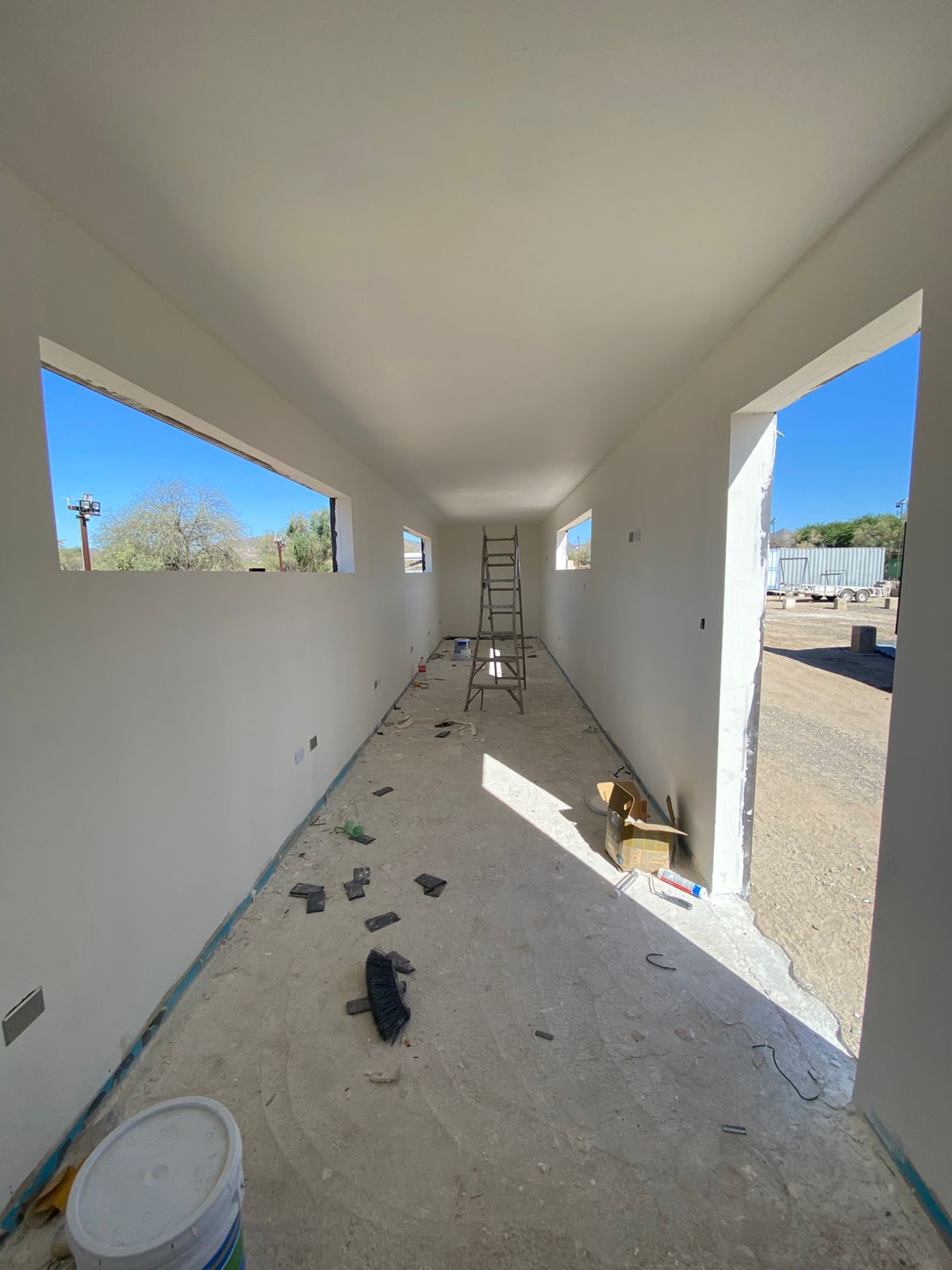 Interior de contenedor del Campus CIAE con tablaroca pintada en blanco, vanos de ventana abiertos y vista al cerro al fondo